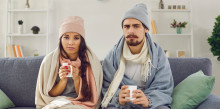Confused looking young couple with blankets and winter hats on while sitting on the couch