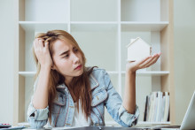 Young woman holding up house model in her hand and looking at it with a skeptical expression