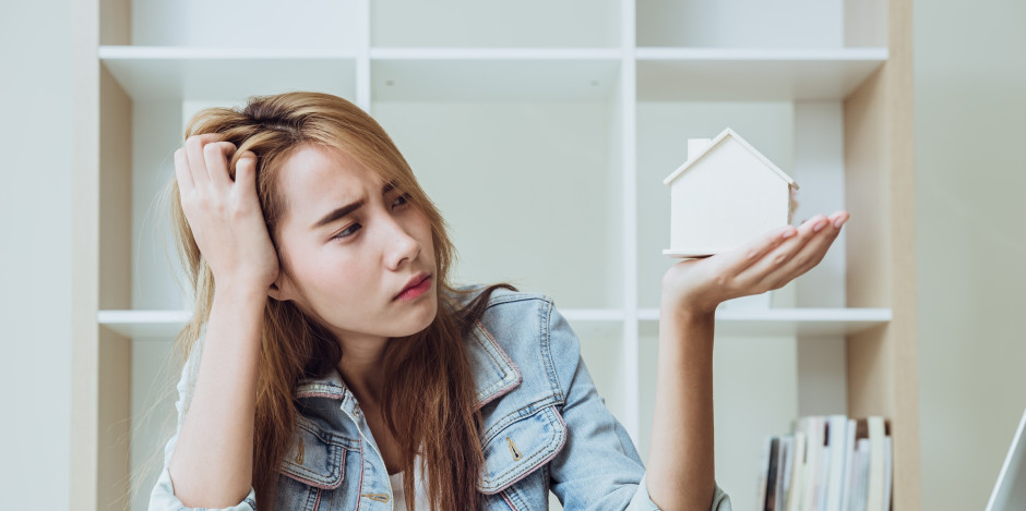 Young woman holding up house model in her hand and looking at it with a skeptical expression
